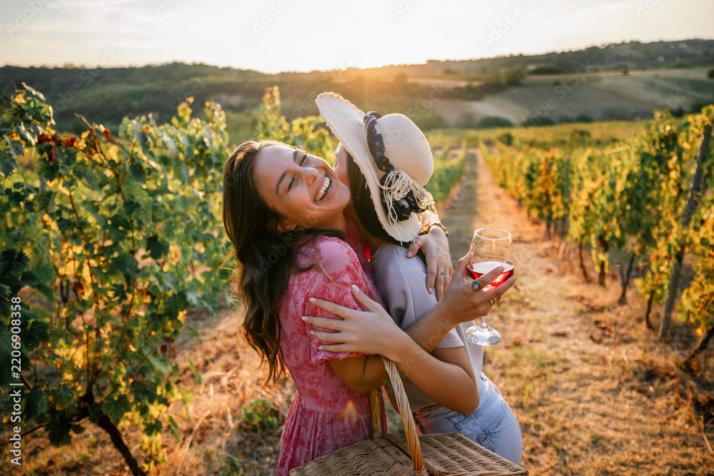 Obraz premium Two joyful female friends hugging tightly with wine in vineyard sunset
