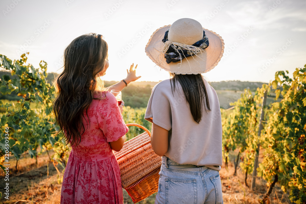 Obraz premium Two women from behind pointing at vineyard sunset landscape
