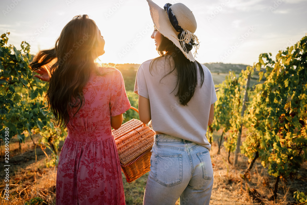 Obraz premium Rear view of two young women strolling through vineyard at golden hour