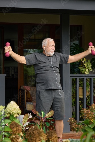 Senior man exercises with dumbbells at home during daylight