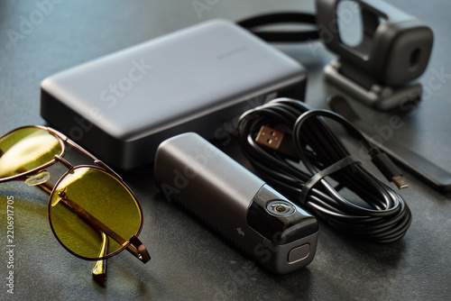 Various tech items including a camera, charging case, sunglasses, and cables on a table