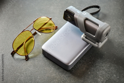Sunglasses and video camera placed on a gray surface with a portable charger in background