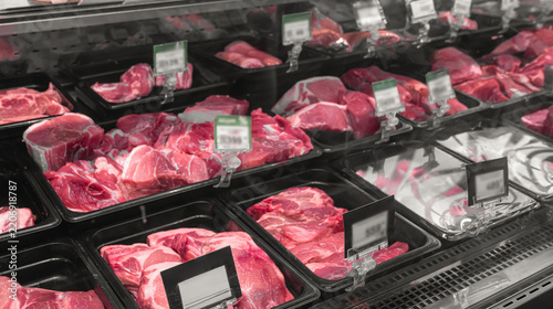 Various cuts of fresh raw meat and beef displayed in a refrigerated supermarket butcher counter with price tags. Meat selection, assortment, pricing, grocery retail and fresh meat shopping concept.