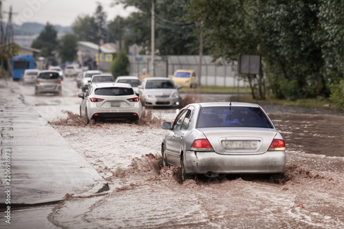 Cars driving through a flooded city road after heavy rain, splashing muddy water during urban flooding and difficult traffic conditions