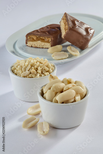 Layered chocolate candy bar with caramel and peanuts broken in half with nut bowls