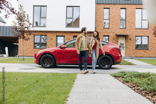 Happy couple walking past electric car in suburban neighborhood