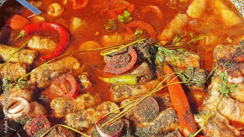 traditional Romanian cabbage rolls - sarmale simmering in a rich, red tomato and pepper sauce garnished with fresh herbs and chili peppers