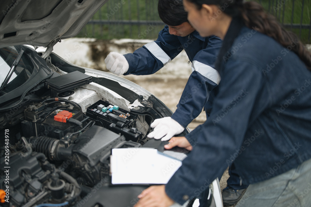 Fototapeta premium Technician explaining electrical system problem in broken car engine under open hood to female driver during roadside insurance check.
