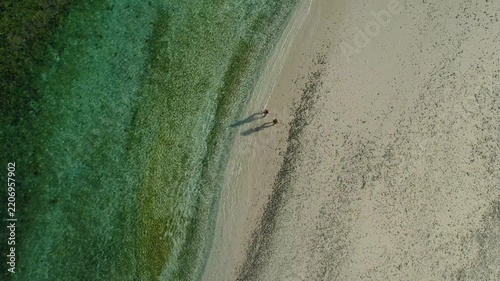 Aerial zenithal view of a young couple holding hands and walking barefoot on the shore of a pristine white sand beach in Coiba National Park, Panama, with crystal clear turquoise water - stock video