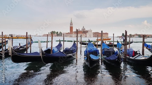 Cinematic view of traditional gondolas moored in Venice with San Giorgio Maggiore church in distance.