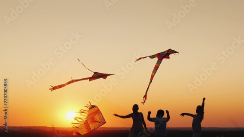 Happy family with children playing with colorful kites in park at sunset, slow motion footage of an active outdoor leisure activity.