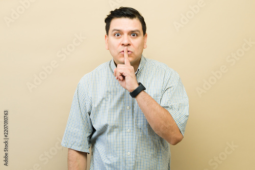Latin man making shush gesture, keeping a secret, asking for silence and quiet, indicating privacy