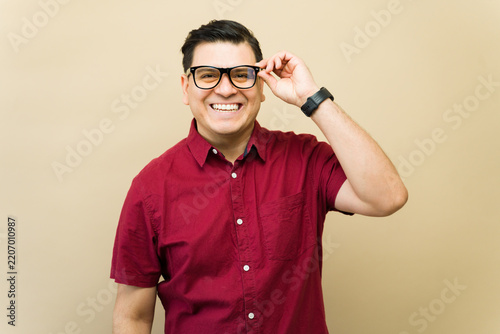 Happy man in red shirt adjusting eyeglasses, smiling brightly at camera, expressing positive emotion and vision