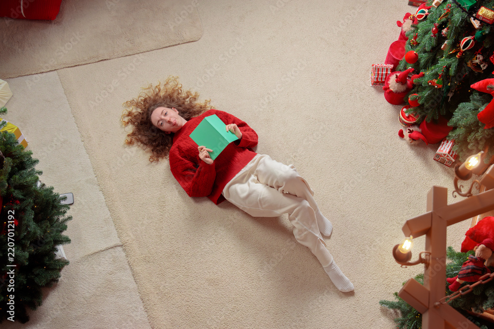 Obraz premium Young woman lying on the floor with a notebook in a cozy festive holiday home environment
