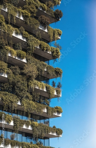 Modern building facade covered in lush green vegetation against a clear blue sky
