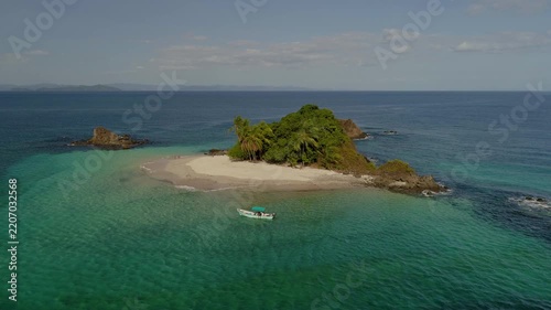 Granito de Oro island with white sand beach and lush vegetation in the clear turquoise waters of the Pacific Ocean, with a small boat anchored nearby, Panama - stock video