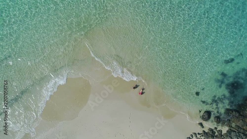 Aerial view showing two people walking on the white sand beach with clear turquoise water of the Pacific Ocean gently washing the shore on Coiba Island, Panama - stock video