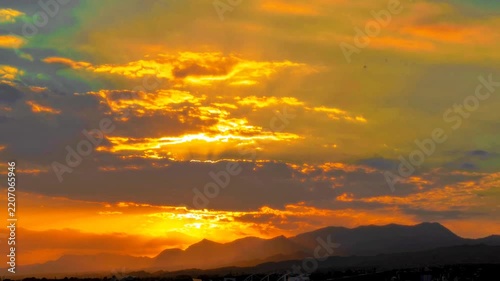 Stunning golden sunset timelapse with dramatic clouds, vibrant orange sky, and dark mountain silhouettes.