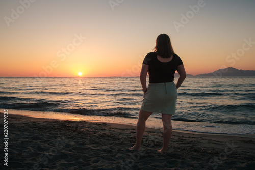A woman standing on a beach on the island of Kos, watching the sunset.