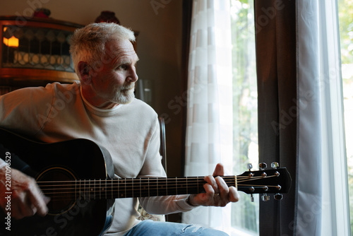 Older man playing guitar by window in a candid moment