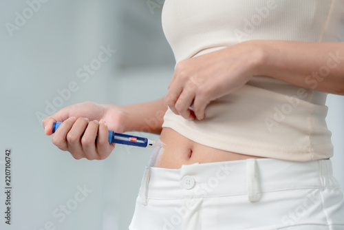 Weight loss medication concept showing a woman holding an injection pen near her exposed abdomen at home, preparing for a self-administered dose, weight management, healthcare, wellness