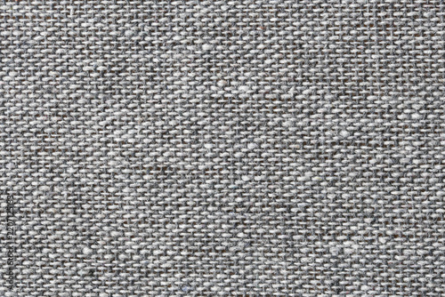 Gray woven fabric closeup. Coarse textile fibers and threads. Neutral upholstery material surface. Detailed woven cloth pattern. Rough textile surface structure. Gray background with visible weave.