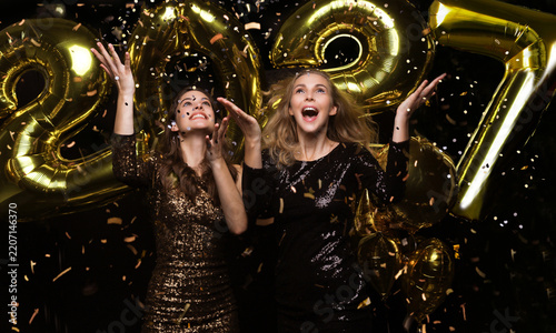 Happy gorgeous girls in stylish sexy party dresses holding gold 2027 balloons, having fun at New Year's Eve Party.