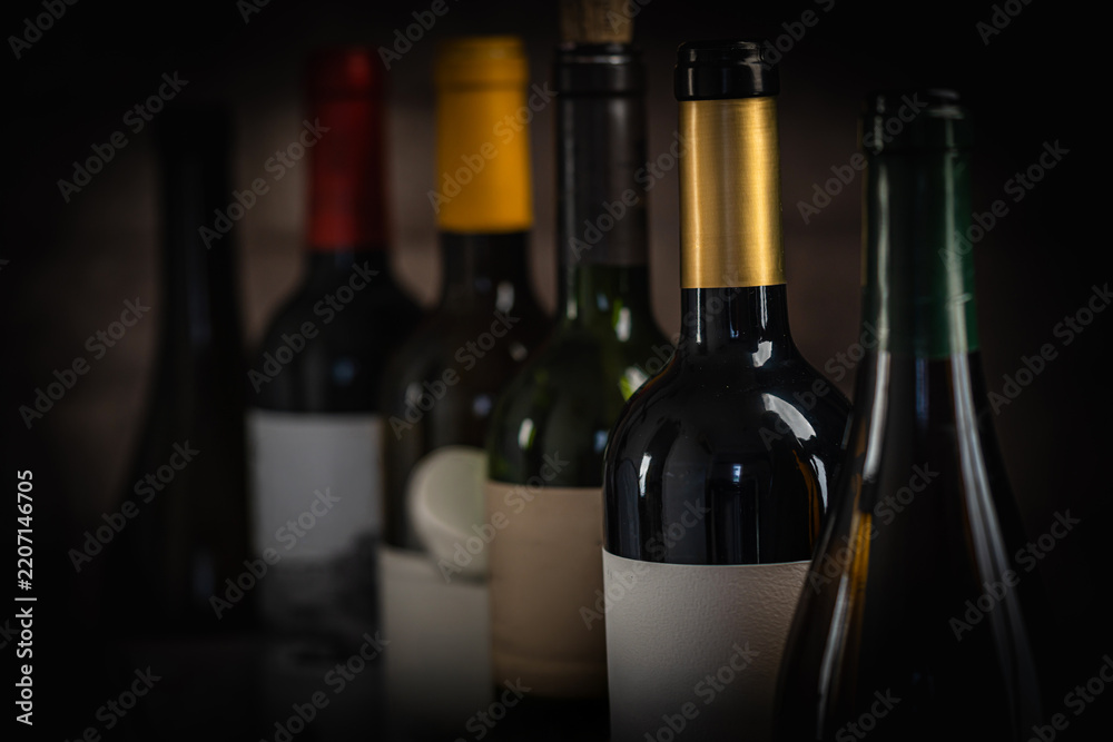 Obraz premium Close-up view of various wine bottles, with a glass of red wine and grapes blurred in the background, creating an elegant and sophisticated wine composition Perfect for wine-themed compositions