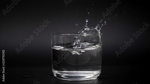 Crystal clear water splashing inside a glass on a dark background, creating dynamic droplets