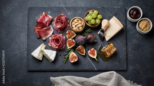 Gourmet Charcuterie Platter with Prosciutto, Brie Cheese, Fresh Figs, Grapes and Honeycomb on a Dark Slate Board