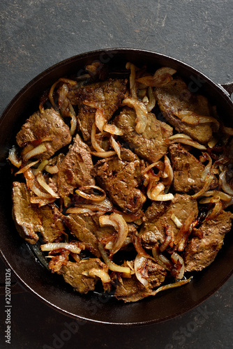 Sauteed liver with butter and onion in pan on black stone background