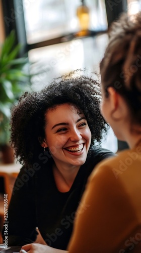 Joyful young woman with curly hair laughing during a conversation with a friend in a cafe