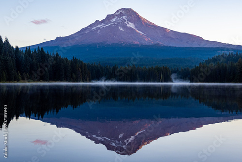Mount Hood reflected in the still waters of Trillium Lake at dawn, with morning mist drifting above the lake and evergreen forest in Oregon