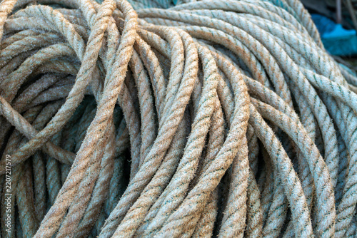 Detailed close-up of thick weathered rope coiled aboard a traditional fishing boat in Portugal. Rough twisted strands create a strong maritime texture associated with fishing equipment, seamanship and