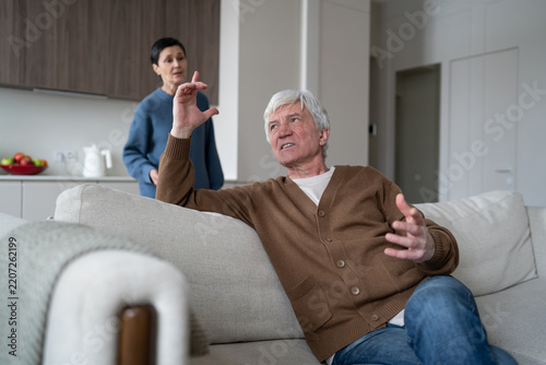Annoyed elderly husband arguing with irritated wife, senior married couple in relationship crisis, distressed man emotionally gesturing and speaking with frustrated older woman, heated home argument.