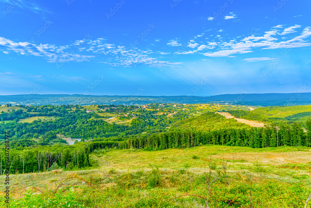 Obraz premium Panoramic view of green forested hills and valleys under bright blue sky with white clouds