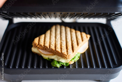 Grilled sandwich with cheese, lettuce and sliced meat cooking in open sandwich press