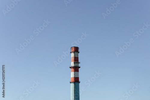 Tall Industrial Chimney Rises Against Clear Blue Sky. Striped Smokestack Marks Factory Infrastructure.