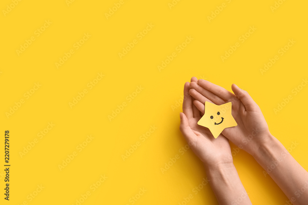 Fototapeta premium Customer satisfaction and positive feedback, hands holding a yellow star with a smiley face for service excellence and quality rating on a yellow background