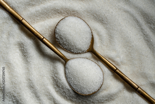 Top view of white refined sugar in two vintage golden spoons forming decorative pattern on heap of granulated sugar. Creative food concept for sweet ingredient or baking