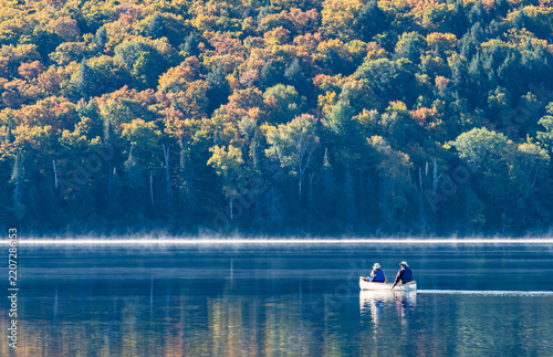 Two People on a White Canoe in a Calm Lake Surrounded by Fall Foliage