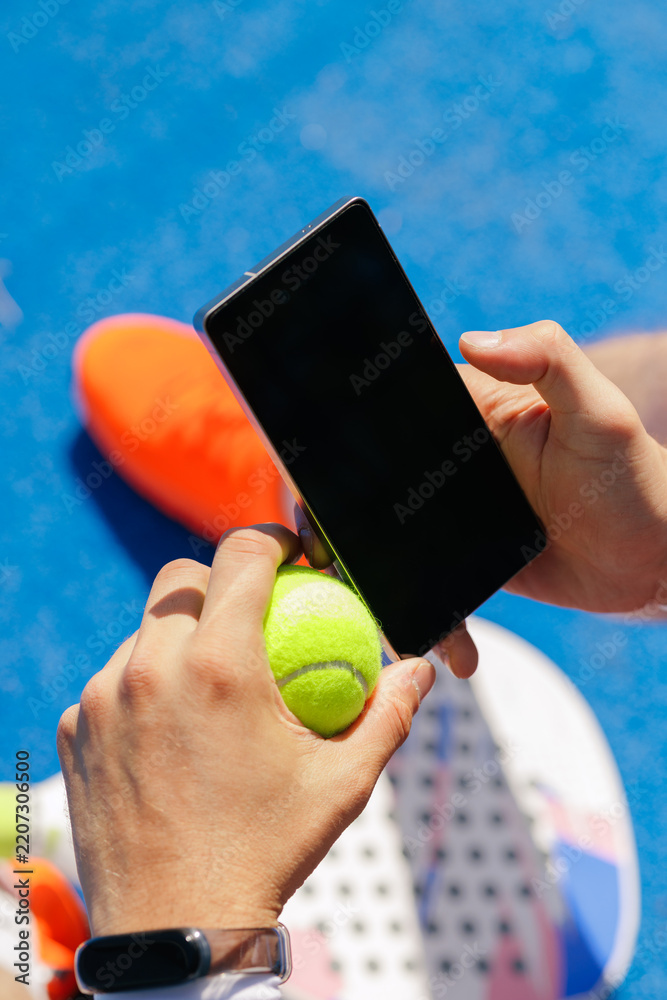 Obraz premium Padel player checking smartphone while holding tennis ball on court