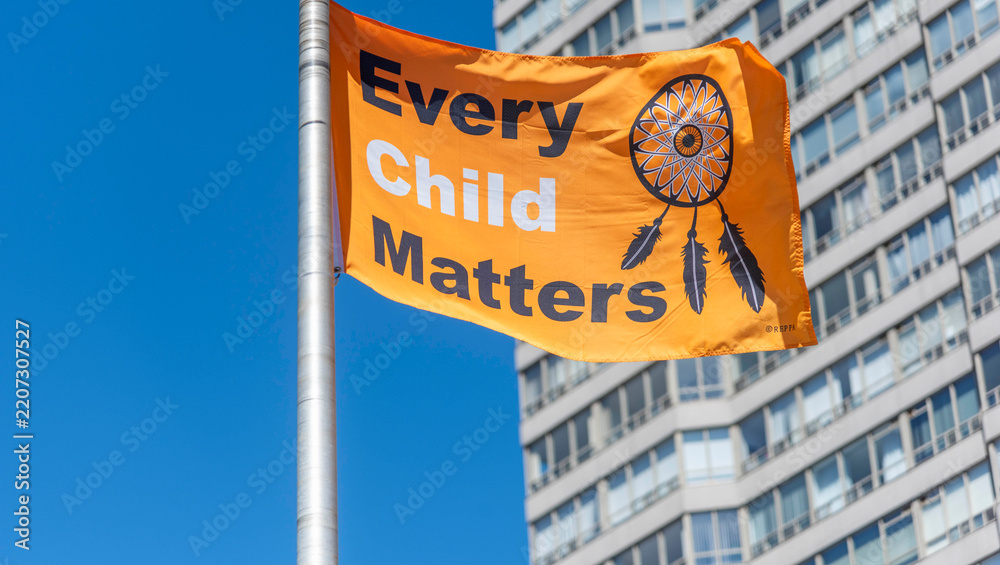 Naklejka premium Toronto Ontario, Canada- July 21st, 2025: An Every Child Matter’s flag on a flag pole flapping in the wind in front of an apartment building. 