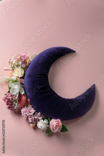 Crescent-shaped pillow with floral decor on a pink surface for a newborn photoshoot; photo background texture.