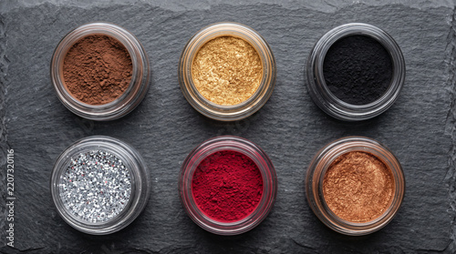 Assorted cosmetic powders and glitters in glass jars on dark slate top view