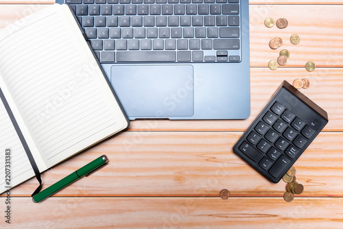 Top view of a laptop keyboard, coins, a pen, and a notebook with blank pages.