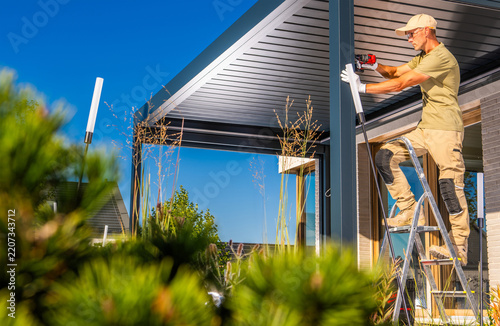 Worker installing a metal pergola from a stepladder