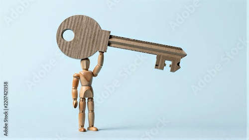 Wooden figure holds giant cardboard key, symbolizing access or unlocking potential.