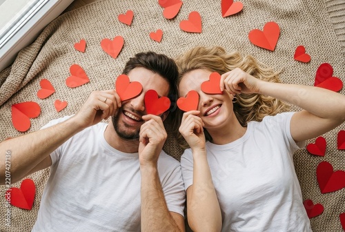 Happy Young Couple Lying on Blanket with Red Paper Hearts Covering Eyes for Valentine's Day Celebration