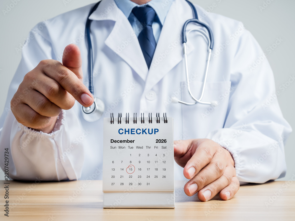 Obraz premium Doctor points to December 2026 desk calendar marked for medical checkup. Year-end preventive healthcare, annual screening, appointment planning and proactive wellness management concepts.